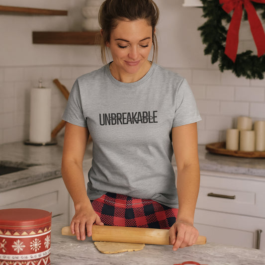 Woman in a kitchen wearing a gray t-shirt with 'UNBREAKABLE' text, rolling out dough.