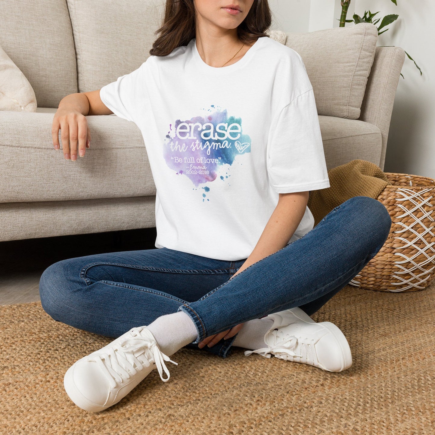 Person wearing a white t-shirt with 'Erase the Stigma' text, sitting on the floor in a living room.