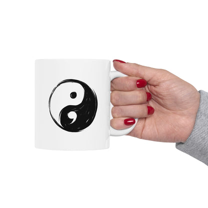 White mug with a black yin yang symbol held by a hand with red nail polish on a white background