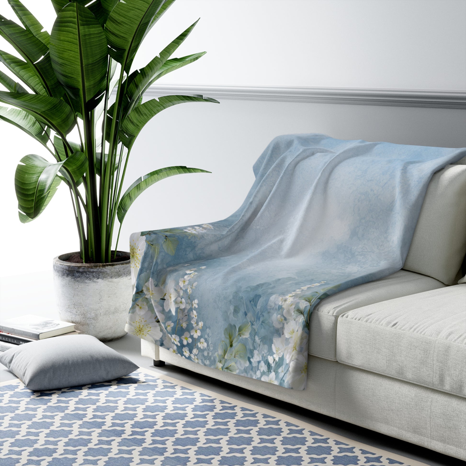 Light blue floral-patterned blanket draped over a white sofa in a living room with a plant and rug.