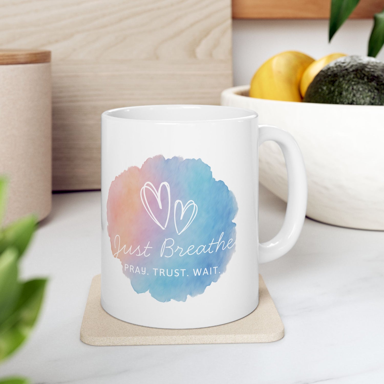 White mug with colorful design and text on a white surface with plants and a plant pot in the background