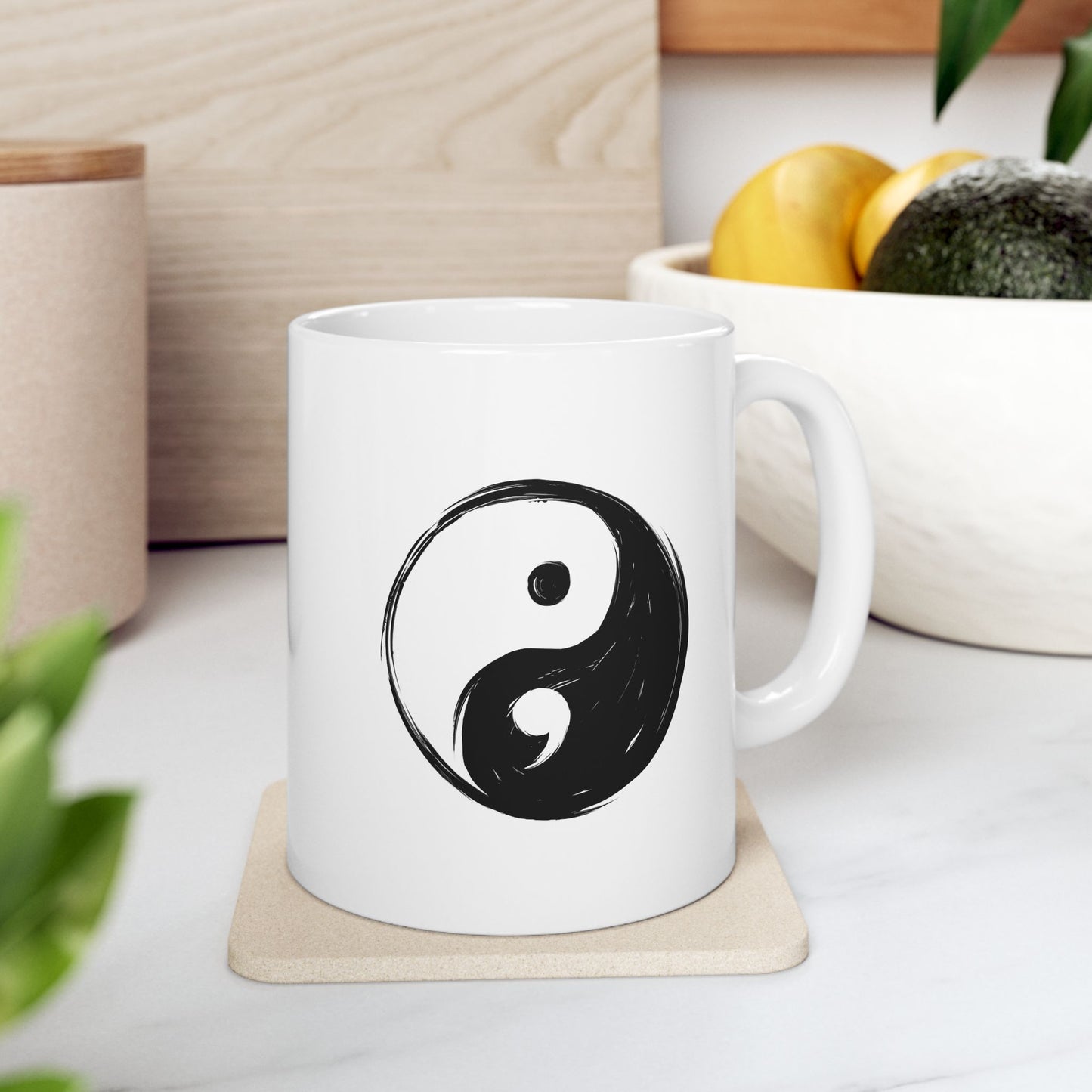 White mug with a black yin yang symbol on a coaster, placed on a light wooden surface.