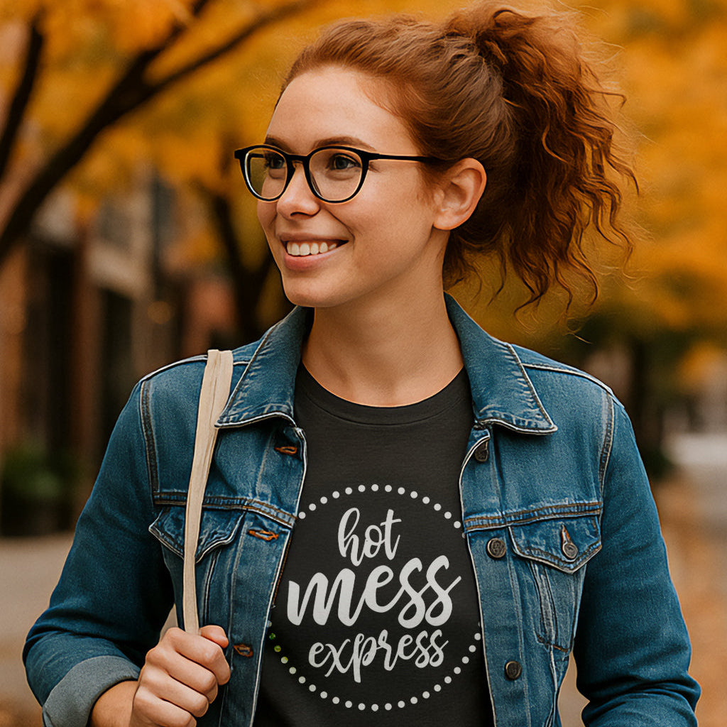 Woman wearing a black t-shirt with 'hot mess express' text, standing outdoors with autumn foliage.