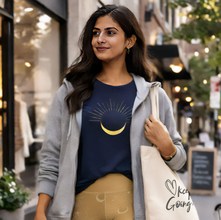 Woman walking on a street wearing a blue shirt with a moon design, gray jacket, and yellow pants.